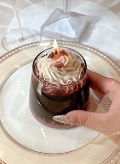 a person holding a small cupcake on a plate with a lit candle in it