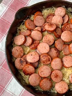 a skillet filled with sausages and rice on top of a red checkered table cloth