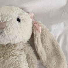 a white stuffed animal with a pink ribbon on its ear and nose sitting on a bed