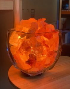 a glass bowl filled with lots of orange rocks on top of a wooden table next to a lit candle