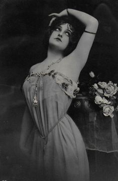 an old black and white photo of a woman in a dress with flowers on her head