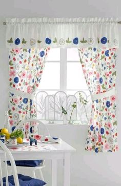 a white table and chairs in front of a window with flowers on the valance