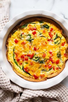 an omelet with tomatoes, spinach and cheese in a white dish on a marble surface