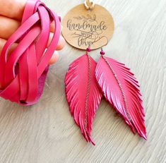 the pink feather earrings are being held up by someone's hand with a tag on it