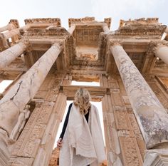 a woman standing in front of an ancient building with columns and pillars on either side