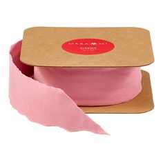 a pink ribbon in a cardboard box with a red label on the front and bottom