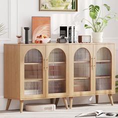 a wooden cabinet with glass doors in a living room next to a potted plant