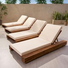 three wooden lounge chairs sitting on top of a cement floor next to potted plants