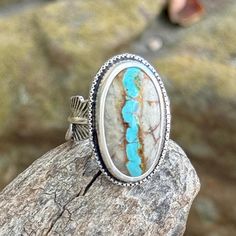 Natural Royston Ribbon Turquoise Sterling silver statement ring Royston Ribbon Turquoise has pulled at my heart strings once again. Usually turquoise is cut so that the face of the stone is all turquoise. For Royston Ribbon, they cut a cross-section, so that you can see the vein of turquoise running through the rock. It mesmerizes me.  This is a glorious piece of natural, untreated ribbon turquoise from the Royston Mine in Nevada. A very striking pattern of turquoise and natural light brown matrix. I used 999 fine silver around the stones, twisted sterling wire, and a feather band. This is a really solid piece that's going to last for generations. The ring measures at a size 8 and is marked .925.  I do not offer resizing for rings. The reason for this is that in order to resize a ring I mu Royston Turquoise Ring, Bohemian Chrysocolla Ring Jewelry, Bohemian Chrysocolla Ring, Adjustable Southwestern Turquoise Ring With Natural Stones, Rustic Sterling Silver Turquoise Ring Gift, Adjustable Chrysocolla Turquoise Ring, Bohemian Chrysocolla Turquoise Ring, Artisan Turquoise Ring With Inlay, Artisan Adjustable Turquoise Ring With Inlay