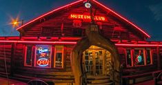 an old wooden building with neon lights on it's roof and stairs leading to the entrance