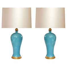 two blue vases with lamps on top of them, one has a gold base and the other has a white shade