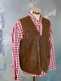 This 1990s brown leather vest has a V neckline, and closes in the front with four snap buttons. The vintage pointed-front Western waistcoat has two pockets on the front, and features topstitching on the leather. The vest has a full beige canvas (cotton) back with a leather half-belt with buckle. Chest = Up to 48 inches (121.92cm) Vest Length (front) = 26 inches (66.04cm) Vest Length (back) = 24 inches (60.96cm) Brand label: Pionier Sportive Size: 46 to 48 US/UK Material: Genuine Leather --- COND Brown Leather Vest, Brown Vest, Mens Vests, Brand Label, Red Button, European Vintage, Leather Vest, Fur Collars, Vintage Men