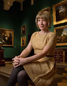 a woman sitting on top of a wooden bench in a room filled with pictures and paintings