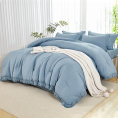 a bed with blue comforters and pillows in a room next to a plant on the floor