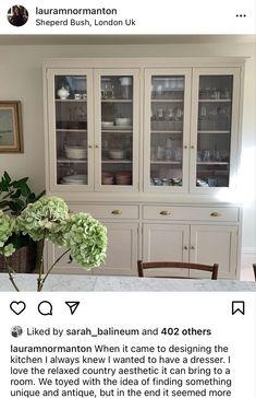 a white china cabinet with glass doors and flowers in the vase next to it on top of a table