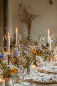 the table is set with candles and flowers in vases, plates and glasses on it