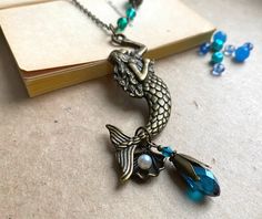 a necklace with a mermaid on it sitting next to a book and some glass beads