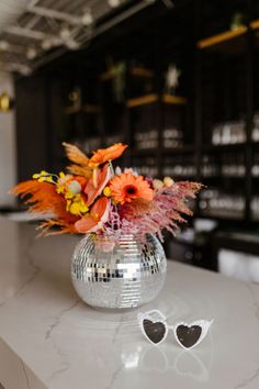 a vase filled with orange flowers sitting on top of a counter next to a pair of heart shaped sunglasses