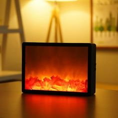 an electric fireplace with red flames in the center on a table next to a lamp