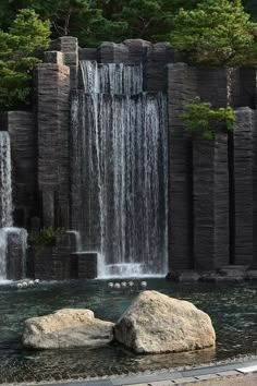 two large rocks sitting in front of a waterfall with water pouring from it's sides