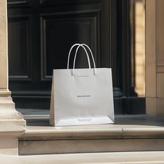 a white shopping bag sitting on the steps of a building with an entrance in the background