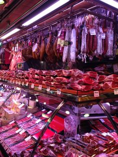 meats and sausages on display in a butcher's shop with lights above them