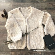 a white sweater sitting on top of a wooden floor next to a black book and pine cone