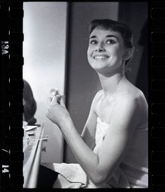 black and white photograph of a woman brushing her teeth in front of a bathroom mirror