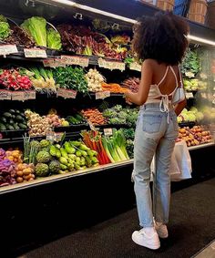 a woman standing in front of a display of fruits and vegetables at a grocery store