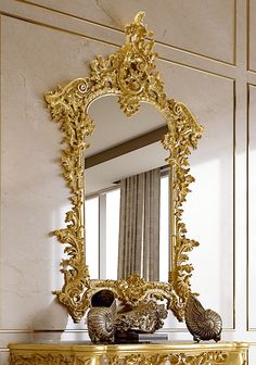 an ornate gold mirror sitting on top of a table next to a vase and two seashells