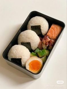 a bento box with rice, sushi and an egg in it on a white surface