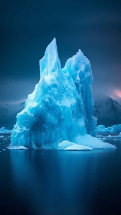 an iceberg floating in the ocean with mountains in the background