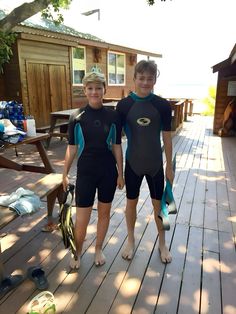 two boys in wetsuits standing on a wooden deck