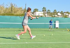 two people playing tennis on a green court with palm trees in the backgrouds