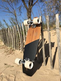 a skateboard leaning against a wooden fence on the sand near a tree and beach