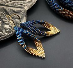 two pairs of blue and gold beaded earrings sitting on top of a black surface