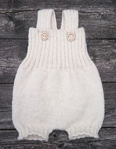 a white knitted baby romper with buttons on the front and bottom, sitting against a wooden background