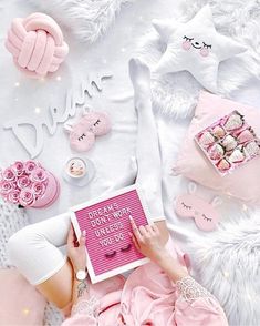 a woman laying on top of a bed holding a pink book next to cupcakes