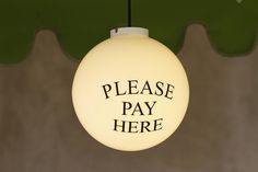 there is a light that says please pay here hanging from the ceiling in front of a green wall