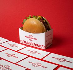 a hamburger sitting inside of a white box on top of red and white paper boxes