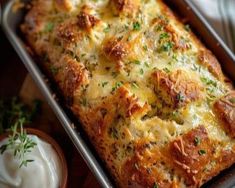 a casserole with cheese and herbs in a baking pan next to some sour cream