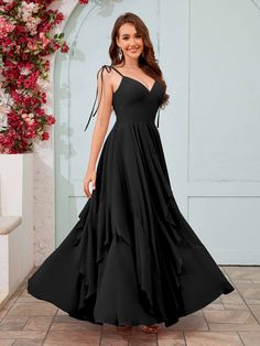 a woman in a long black dress standing on a tile floor with flowers behind her