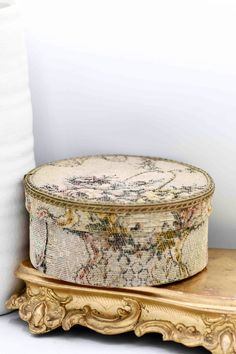 an old hat box sitting on top of a wooden stand next to a roll of toilet paper