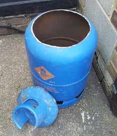 a blue barrel sitting on the ground next to a trash can and an empty plastic cup