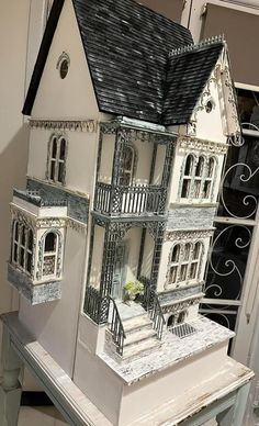 a white doll house sitting on top of a table next to a black and white fence