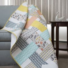 a couch with a quilt on it next to a table and chair in the background