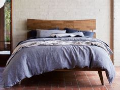 a bed with blue linens and pillows in a room next to a brick wall