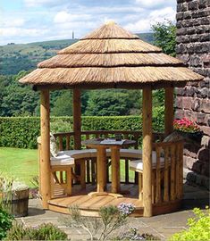 a wooden gazebo sitting on top of a lush green field next to a stone wall