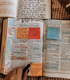 an open bible with sticky notes on it and someone holding a pen in their hand