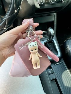 a hand holding a keychain with a cartoon bear on it in a car